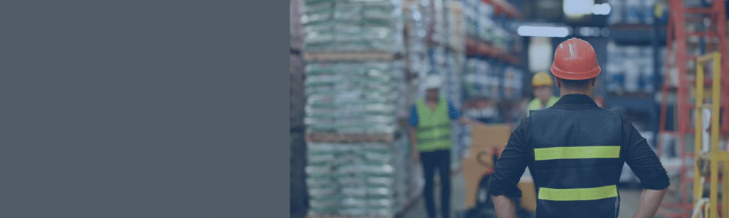 Man in a hard hat looking down an aisle in a warehouse.